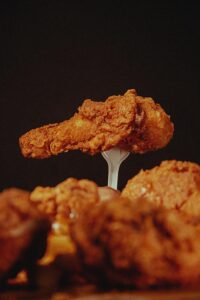 Close-up of a crispy fried chicken wing held aloft by a fork against a dark background.