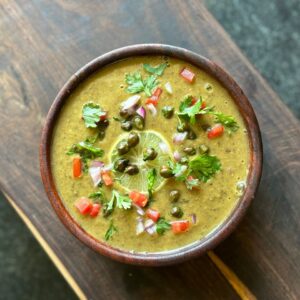 A vibrant bowl of traditional Indian lentil soup garnished with fresh coriander, chili, and lime.